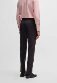 Roze lang evoluerend shirt gedragen met donkere broeken, met een eenvoudig en strak ontwerp. Shirt heeft knoopmanchetten en een getailleerde pasvorm.