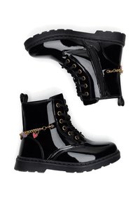 Botines de charol negro con cordones en la parte delantera, ojales dorados, cremallera lateral y una cadena con charms de corazones de colores. Suela de goma.