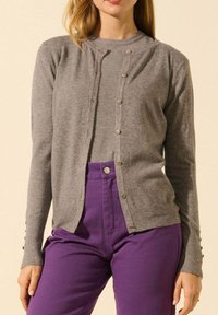 Cardigan gris avec un col rond et une fermeture par boutons sur le devant. Fabriqué en matériau doux, il présente des détails de boutons sur les manches et une coupe décontractée.