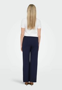 Tumed laiused püksid elastse vöökohtaga, koos valge hästi istuva T-särgiga. Sile tekstuur, ilma nähtavate mustriteta, minimalistlik disain.