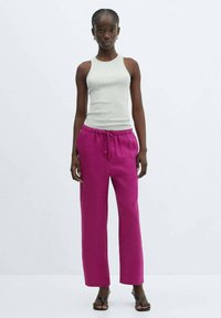 Light gray fitted tank top paired with relaxed, bright pink linen pants that have an elastic waistband and drawstring detail. Black sandals.