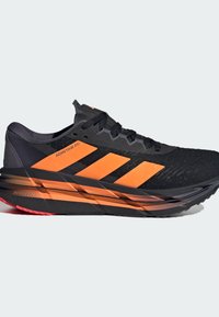Black running shoe with orange accents, mesh and synthetic upper, textured surface, and cushioned sole with red details and three stripes logo.