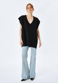 Top negro de punto oversized con escote en V profundo, mangas cortas y un corte relajado, combinado con jeans de mezclilla acampanados de color azul claro y tacones negros.