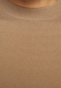 Suéter de punto marrón con un cuello redondo acanalado y una textura suave. La tela parece blanda y ajustada al cuerpo, con un color uniforme.