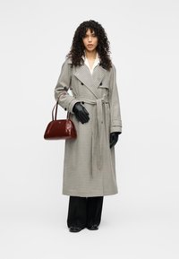 Γκρι καρό παλτό τύπου trench με διπλή σειρά κουμπιών, ζώνη στη μέση, συνδυασμένο με μαύρα γάντια, μαύρο παντελόνι και μπορντό τσάντα.