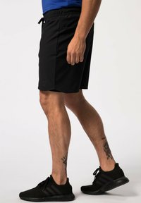 Czarne szorty sportowe z elastycznym paskiem i sznurkiem. Posiadają elegancki design i praktyczne boczne kieszenie. Noszone z czarnymi butami sportowymi.