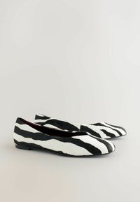Les ballerines à imprimé zèbre présentent un design texturé noir et blanc, avec une semelle basse et un bout arrondi. L'intérieur est d'un bordeaux foncé.