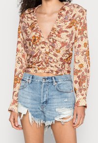 Blusa con motivo floreale e scollatura a V profonda, abbinata a pantaloni shorts in denim strappati con orli sfrangiati e lavaggio chiaro.