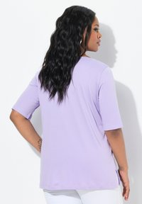 T-shirt di colore lilla realizzata in tessuto morbido, con maniche corte, scollatura rotonda e spacco laterale per facilitare i movimenti.