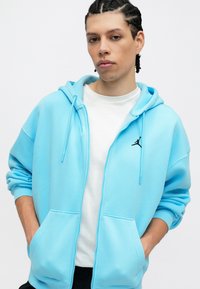 Ανοιχτό μπλε φούτερ με φερμουάρ μπροστά, διαθέτει μαύρο λογότυπο Jordan στη θήκη, δύο μπροστινές τσέπες και άνετη εφαρμογή.