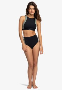 Schwarzes Sportbikini mit grünen Akzenten. Hohe Taille und ärmelloses Crop-Top-Design. Glattes, elastisches Material mit einer enganliegenden Silhouette.