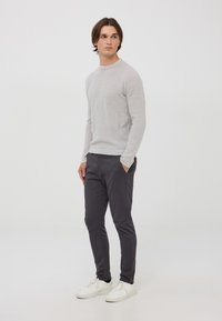Maglione a coste grigio chiaro, design attillato. Pantaloni slim-fit grigio scuro, in misto cotone. Sneakers bianche con chiusura con lacci, texture liscia.
