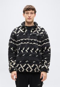 Μπλούζα από φλις σε ασπρόμαυρο με μοτίβο, με γιακά μισού φερμουάρ. Διαθέτει υφασμένη επιφάνεια και ένα λογότυπο στο στήθος.