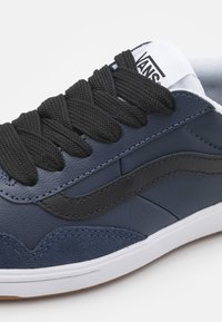 Sapatilha azul-marinho com couro texturizado e camurça, apresentando atacadores pretos e uma etiqueta de logo branca. Perfil baixo com sola de borracha.