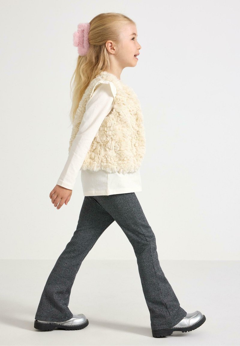 Creme faux fur vest over en hvid langærmet bluse, parret med mørkegrå flared bukser og skinnende sølv sko. Pink hårtilbehør inkluderet.