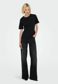 Sort kortærmet top med rund hals og en glat tekstur, parret med højtaljede sorte brede jeans.