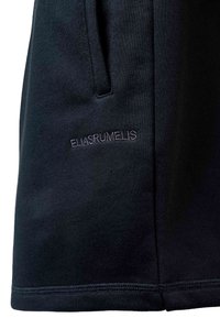 Gros plan sur un tissu noir avec une poche latérale cousue et "ELIASRUMELIS" brodé en fil blanc.