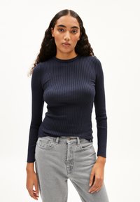 Marineblaues, geripptes Langarmoberteil mit rundem Ausschnitt, kombiniert mit hellgrauen Jeans. Der Stoff hat eine glatte Textur und ein eng anliegendes Design.