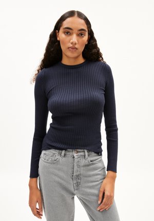 Marineblauwe ribgebreide top met lange mouwen en een ronde halslijn, gecombineerd met lichtgrijze jeans. De stof heeft een gladde textuur en een aansluitend ontwerp.