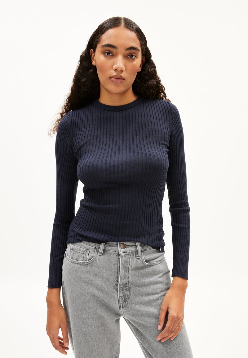 Marineblaues, geripptes Langarmoberteil mit rundem Ausschnitt, kombiniert mit hellgrauen Jeans. Der Stoff hat eine glatte Textur und ein eng anliegendes Design.