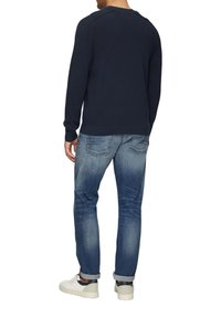 Marineblauwe gebreide trui met een ronde halslijn, gecombineerd met lichtblauwe denim jeans. De schoenen zijn wit met zwarte accenten en hebben opgerolde boorden.
