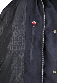 Marineblauwe jas met een gladde buitenkant, een ritszak versierd met rood en wit, en een gestreepte binnenzijde met herhaalde logo's.