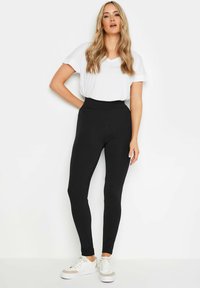 Leggings neri a vita alta con una texture liscia e elastica, abbinati a una t-shirt bianca a V e sneakers bianche.