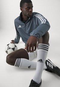 Gray athletic jacket with white stripes, black soccer cleats, white socks with black stripes, and a black and white soccer ball.
