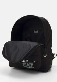 Zaino nero con compartimento principale con cerniera, dotato di tasca frontale con patta e tasca interna con cerniera. Logo EA7 sulla parte anteriore.