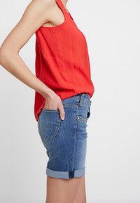 Red sleeveless top and denim shorts. The shorts are blue, cuffed at the hem, with two back pockets and a fitted design.