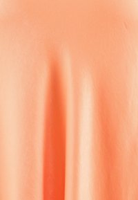 Tissu doux et texturé dans une teinte corail clair, avec une surface lisse et une drapée douce créant des plis et des ombres subtiles.