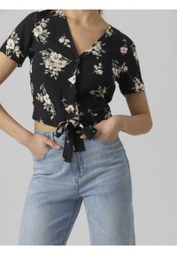 Svart blommig kortärmad blus med v-ringning, knappstängning och knytning i midjan, tillsammans med ljusblå högmidjade jeans.