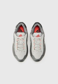Sive i bijele atletske cipele s mrežastim gornjištem, teksturiranim detaljima i svijetloružičastim vezicama. Istaknuti Adidas logo na jeziku.