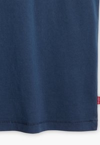 Marineblå bomulds T-shirt med en glat tekstur, der har en lige kant og et lille rødt logolabel på siden.