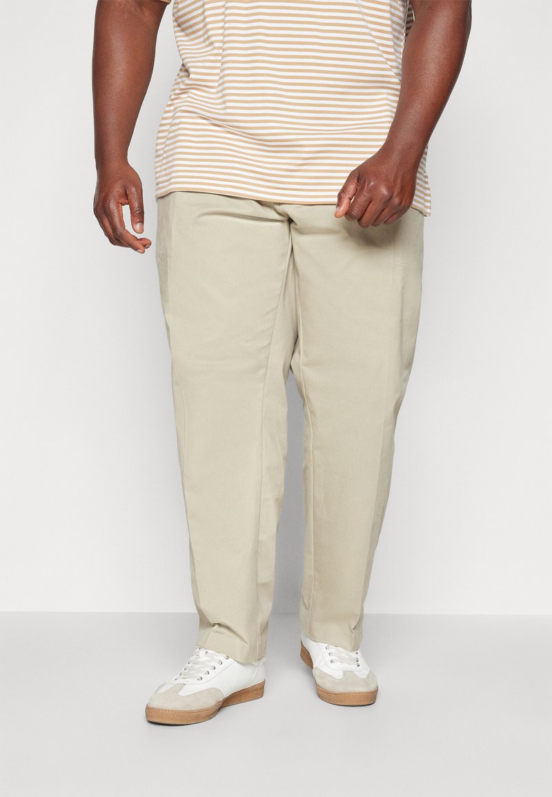 Chino beige con vestibilità dritta, realizzati in tessuto morbido. Abbinati a sneakers bianche con dettagli beige e una camicia a maniche corte a righe.