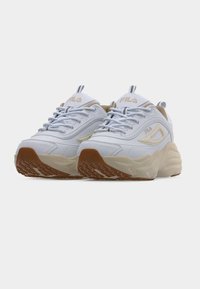 Λευκά και μπεζ chunky sneakers FILA με παχιές σόλες και καφέ εξωτερικές σόλες με σχέδιο, εμφανίζονται από χαμηλή μπροστινή γωνία σε λευκό φόντο.