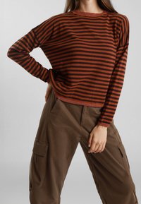 Maglione a righe in arancione bruciato e nero, con maniche lunghe, scollo a costine e una vestibilità ampia, abbinato a pantaloni cargo marroni.