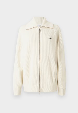 Krémový žebrovaný pletený cardigan na zip s širokým límcem, zapínáním na zip a decentním logem na levé hrudi. Texturovaná tkanina.