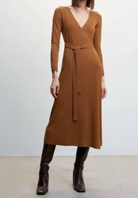 Robe longue à côtes dans une teinte marron chaud, avec un décolleté en V profond, des manches longues, une ceinture assortie à la taille et une longueur midi évasée.