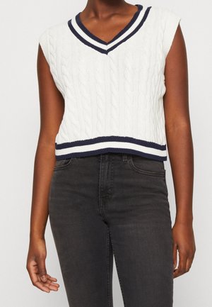 Pull sans manches en tricot blanc avec un col en V, orné de rayures bleu marine le long du col et de l'ourlet. Longueur cropped.