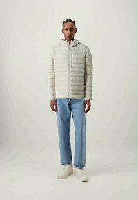 Helehall puffer-jakk, millel on kapuuts, millel on horisontaalne tikand, lukuga sulgemine ja eesmine tasku. Kanda koos siniste teksade ja valgete tossudega.