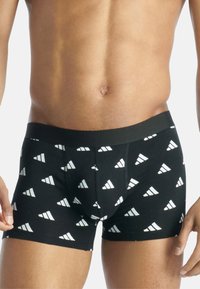 Svarta boxerkalsonger med vita triangulära mönster, mjuk tyg, elastisk midja, åtsittande design och korta ben.