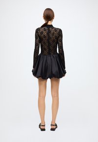 Black lace bodysuit with long sleeves, contrasting satin bubble skirt. Back zipper closure, smooth fabric texture, sheer floral pattern.