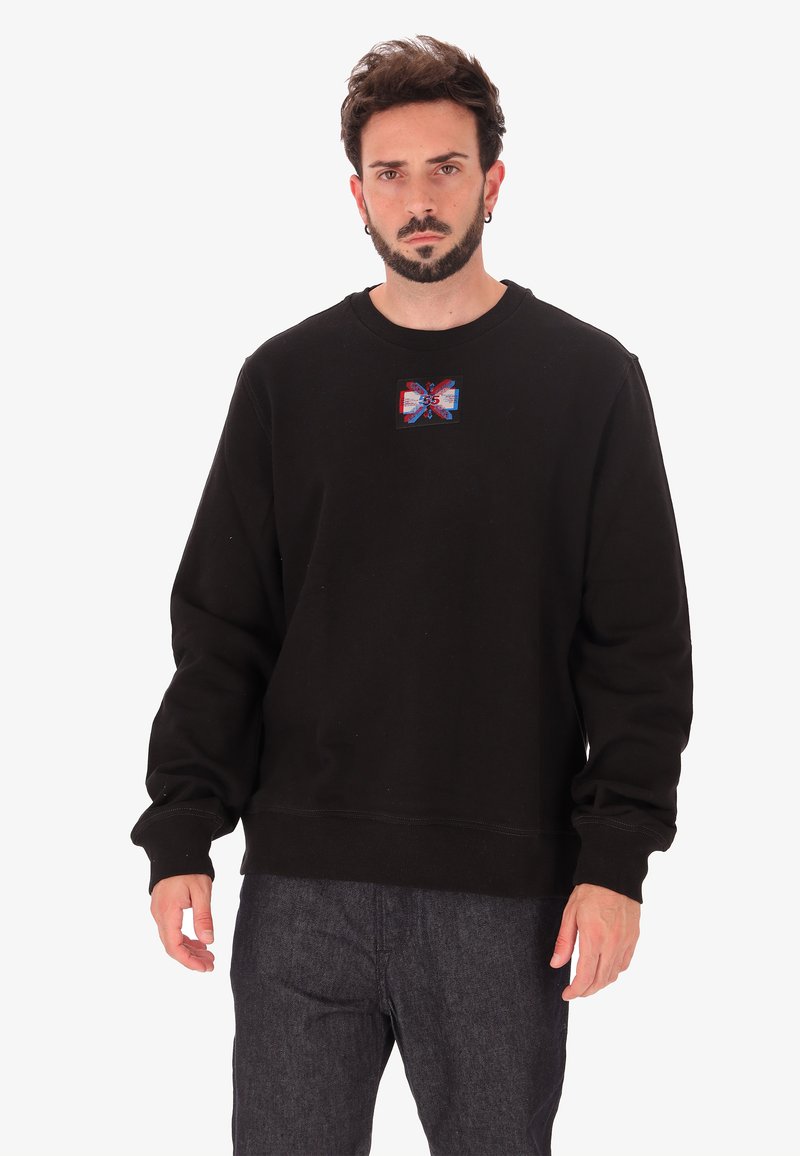 Felpa nera con scollo a barca, caratterizzata da una patch grafica colorata sul petto. Il design include accenti rossi e blu.