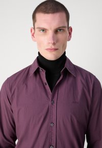 Donker paarse overhem shirt met een subtiele textuur en een klein logo, gecombineerd met een zwarte coltrui eronder.