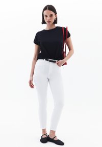 Camiseta negra de manga corta, jeans skinnies blancos, zapatos negros trenzados y un bolso cruzado rojo. Diseño simple y silueta ajustada.