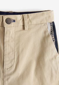 Beige Baumwoll-Twill-Shorts mit Knopfverschluss, ausgestattet mit marineblauen Akzenten und seitlichem Detail mit Text, gefertigt für Komfort und Langlebigkeit.