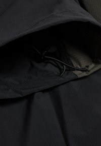 Nahaufnahme eines schwarzen Stoffes, der eine Kapuze mit einem verstellbaren Kordelzug und sichtbaren Nähdetails am Innenfutter zeigt.