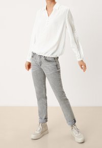Blusa bianca a maniche lunghe, texture con colletto e patta dei bottoni, abbinata a jeans slim-fit grigi chiari e sneakers con platform beige.