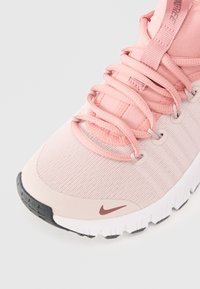 Scarpa sportiva Nike con tomaia in mesh rosa chiaro, lacci in tessuto morbido, suola in gomma e puntale di colore grigio scuro a contrasto.